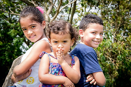 close-up photo of two girls and boy standing beside green trees during daytime thumbnail
