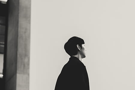 grayscale photo of man in coat standing near building thumbnail