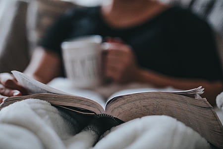 man holding white ceramic mug while reading book thumbnail