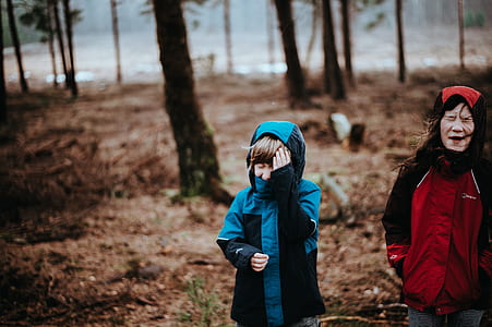 girl wearing red hoodie jacket standing near boy in blue jacket walking on forest thumbnail