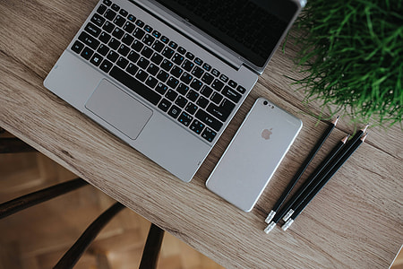 Silver Acer laptop on a wooden desk with a green plant, pencils and an Apple iPhone thumbnail