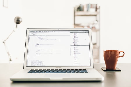 turned-on MacBook Pro on brown desk beside brown mug thumbnail
