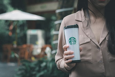 selective focus photo of woman wearing pink shirt holding white and black Starbucks cup with her right hand thumbnail