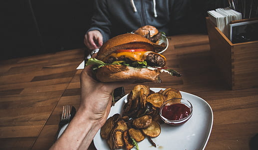 person holding hamburger with sliced tomato, lettuce, and cheese thumbnail