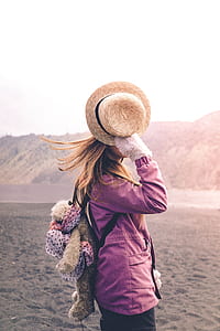 woman standing on sand holding hat during daytime thumbnail