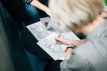 woman in gray top holding blue pencil while drawing on white paper thumbnail