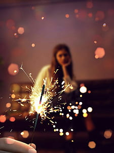 close-up photo of person holding firecracker overlooking woman sitting on chair thumbnail