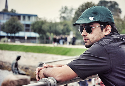 man wearing black aviator-style sunglasses leaning on gray stainless steel railings outdoor during daytime thumbnail