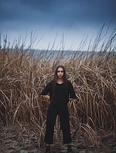 woman standing with hands behind her back in front of brown dried tall grasses thumbnail