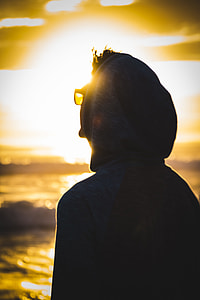 silhouette person wearing hoodie and sunglasses during golden hour photo thumbnail