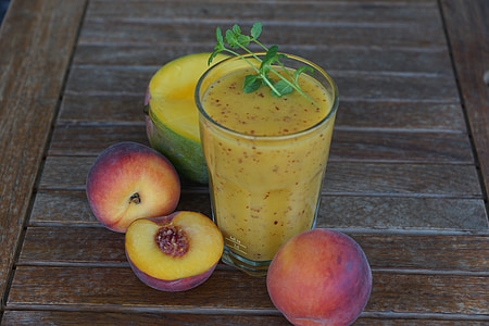 sliced peaches on brown surface beside drinking glass with yellow liquid and herb on top thumbnail