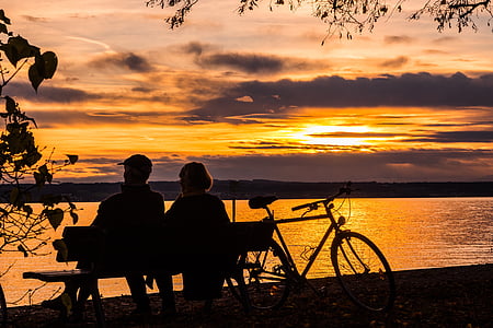 silhouette of man and woman sitting on bench facing body of water thumbnail
