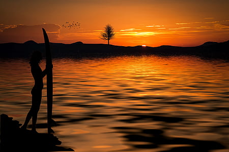 silhouette of woman holding surfboard during sunset thumbnail