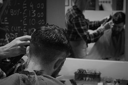 grayscale photography of man cutting man's hair in front of mirror thumbnail