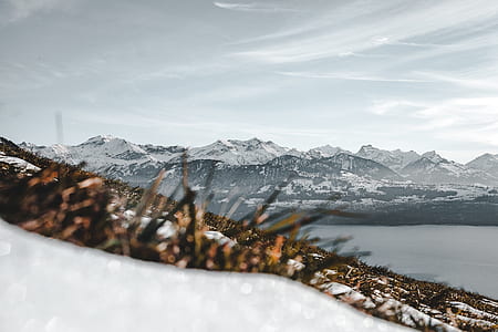 overlooking view of snowy mountain surrounded by body of water under white clouds thumbnail