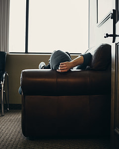 person lying on brown leather sofa near window thumbnail