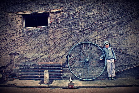 boy in gray hoodie standing beside penny-farthing spoke leaned on gray wall thumbnail