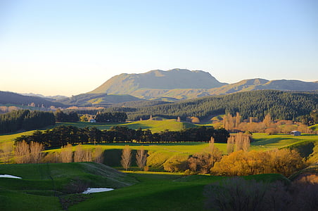 green grass field and mountain at distance under blue sky thumbnail