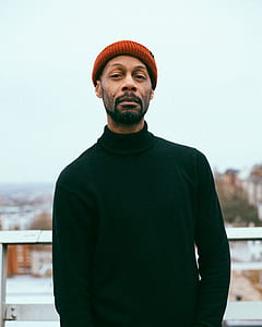 man wearing green turtleneck sweater and orange knit hat thumbnail