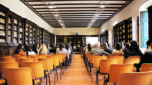 group of people sit on brown chairs inside white painted hall thumbnail