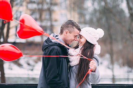 woman holding a heart balloon facing a man with black jacket during daytime thumbnail