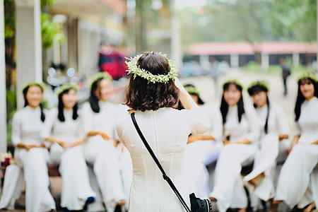woman taking photo of women sitting on bench near building thumbnail