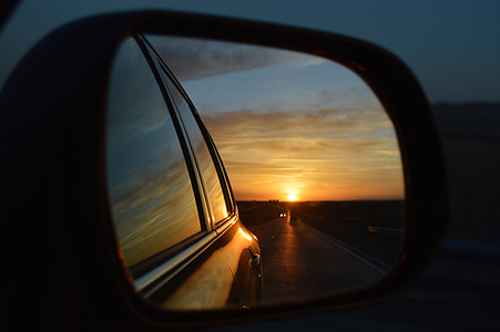 vehicle side mirror showing following vehicle on road during sunset thumbnail