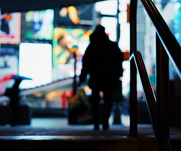 silhouette photography of person walking near post and building with LED screens thumbnail