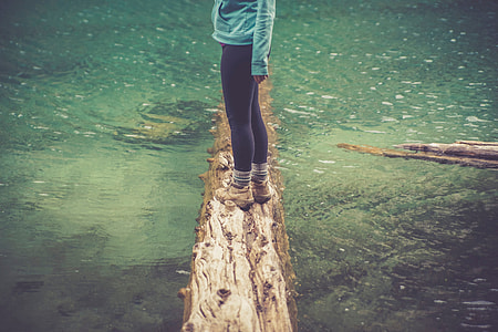 woman in black leggings standing on withered tree log on river thumbnail