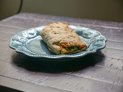 Spinach, feta cheese, and egg all wrapped in a tortilla. Sitting on a blue plate in the sunlight. thumbnail