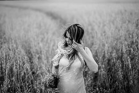 grayscale photo of woman in grass field holding her hair while looking sideways thumbnail