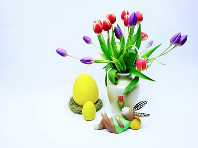 red and purple tulip flowers in white ceramic vase beside yellow egg toys thumbnail