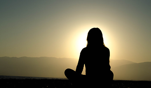 person sitting near body of water in front of mountain ranges thumbnail
