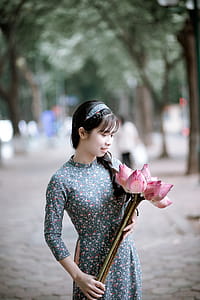 Woman Holding Pink Lotus Flowers Bouquet on Road Beside Green Trees thumbnail