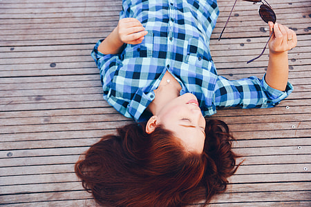 woman in blue, white, and grey plaid long-sleeve shirt lying on brown wooden surface thumbnail