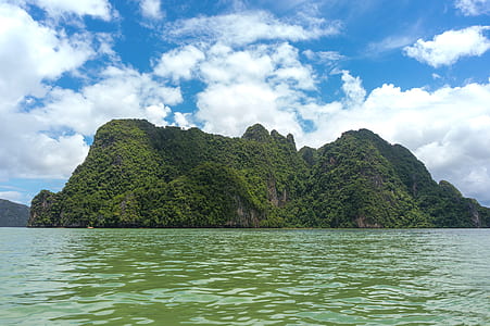 landscape photography of island surrounded by sea water under cloudy sky thumbnail
