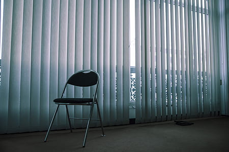 black and gray folding chair in front of white window blinds thumbnail