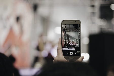 selective focus photography of person holding smartphone displaying male group playing drum instrument thumbnail