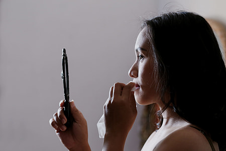 woman holding tissue and mirror wiping her lips thumbnail