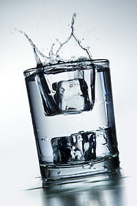 clear glass filled with water and two ice cubes spilling out thumbnail
