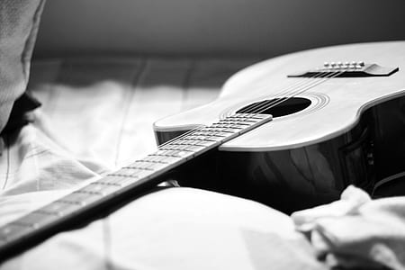 Gray Scale Photography of Acoustic Guitar on Bed thumbnail