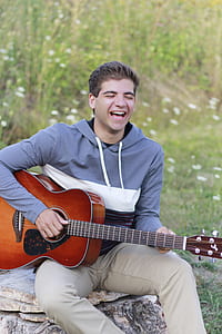 man playing guitar sitting on brown rock during daytime thumbnail