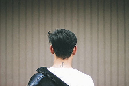 man wearing white shirt and black jacket facing brown wall thumbnail