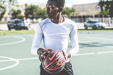 man wearing white long-sleeved shirt holding red and black Nike Kevin Durant basketball on basketball court thumbnail