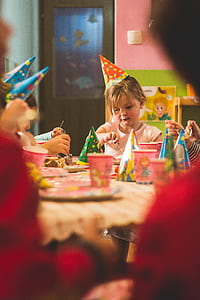 girl wearing party hat sitting in front of table together with other children thumbnail