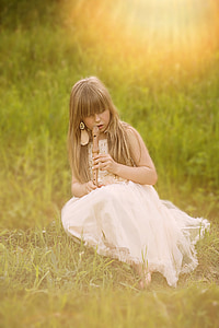 girl sitting on grass while playing wooden flute thumbnail