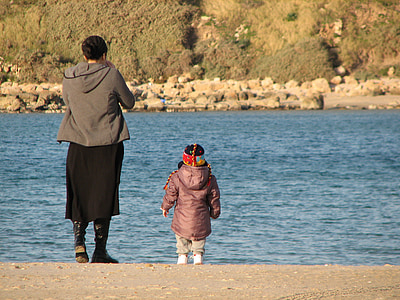 woman and girl on brown sand near body of water during daytime thumbnail
