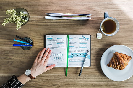 person holding an opened book on table beside a cup of tea thumbnail