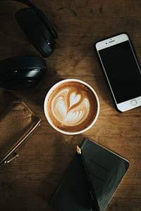 white ceramic cup filled with coffee with coffee art beside silver iPhone 6 thumbnail