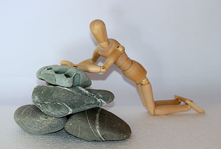 wooden doll leaning on stack rocks thumbnail